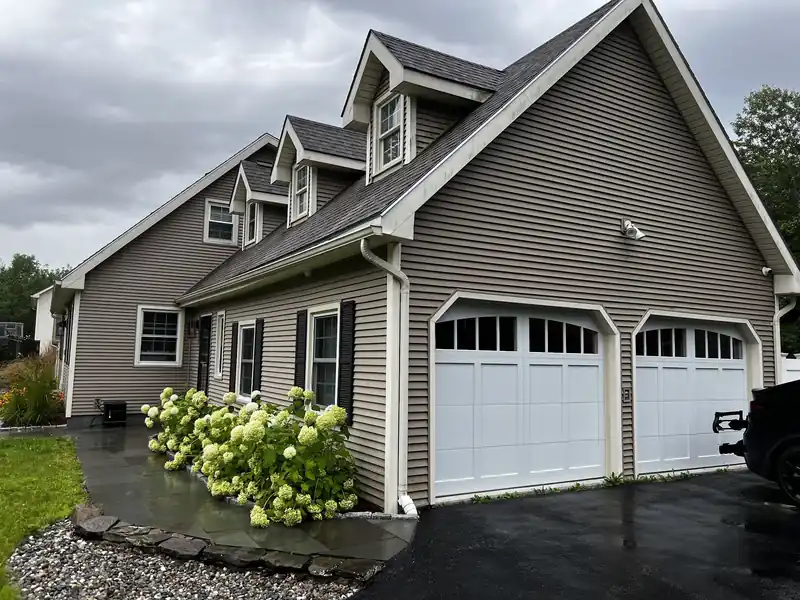 Customer photo of a grey house with two white windowed carriage doors and hydrangeas