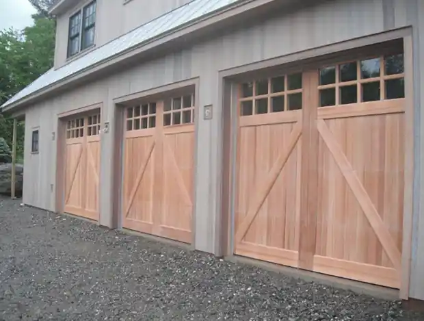 Three dark carriage-house doors with X-brace and windows on a gravel drive