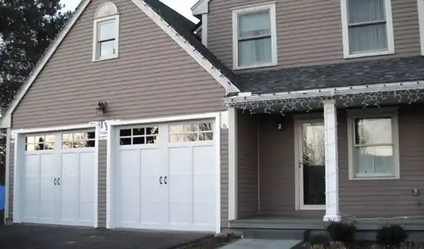 Two white carriage doors on a taupe house with a porch