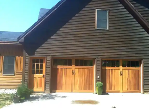 Two dark carriage doors on a brown-shingled house, entry door at left