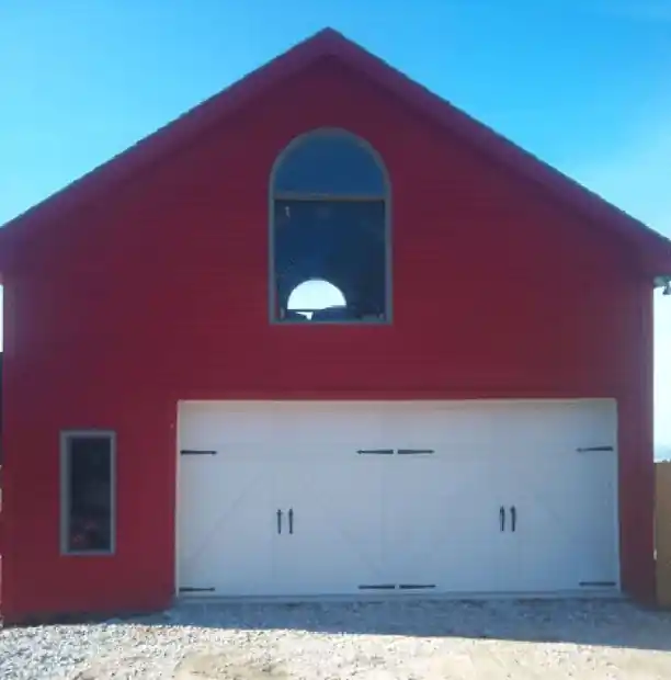 Red barn gable with a wide white carriage door and an arched window above