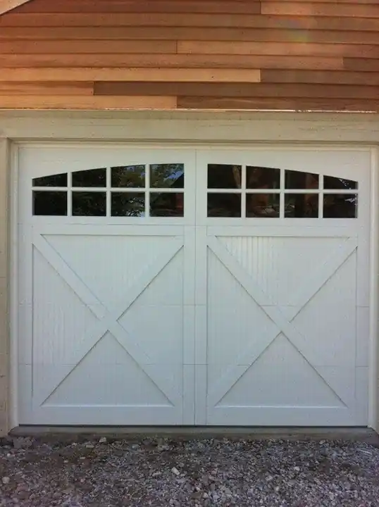 Close view of a white X-brace door with an arched window row against cedar siding