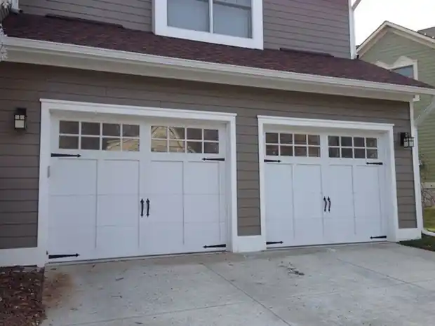Two white carriage doors on grey-brown siding with a concrete apron