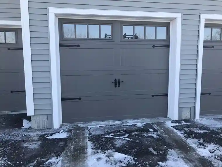 Grey door with black hardware in a white-trimmed opening on a snowy drive