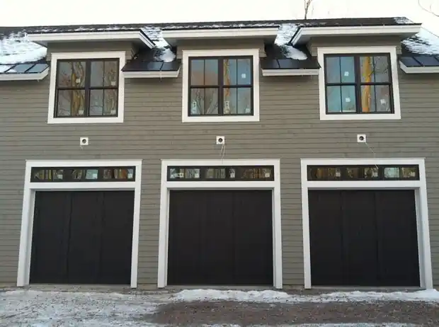 Three dark doors under a row of transom windows on grey-green siding