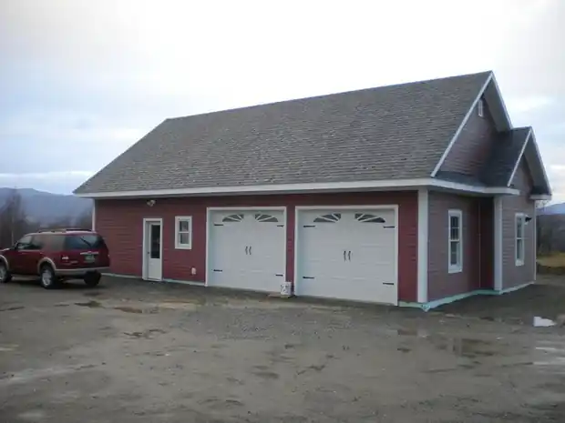 Red-sided detached garage with two white arched-window doors and a red SUV in the yard