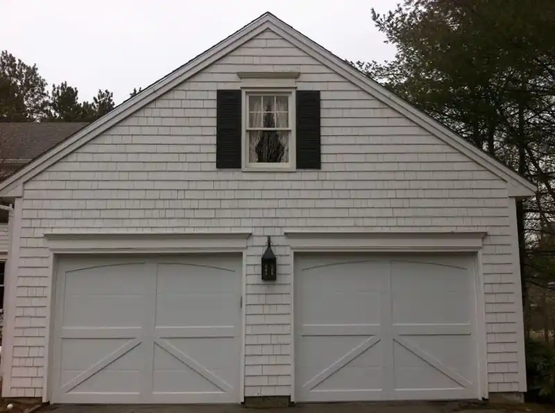 Two grey-white carriage doors under a cedar shake gable with black shutters