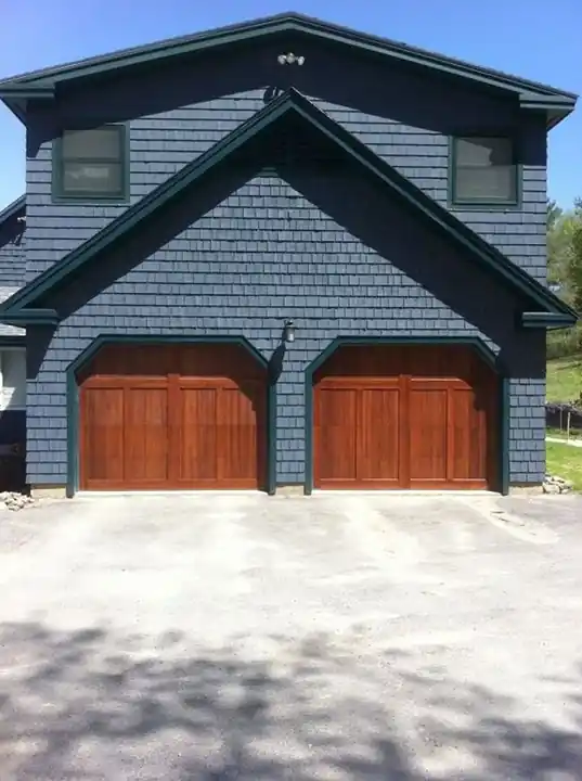Two dark arched-top doors on a blue shingle house with green trim