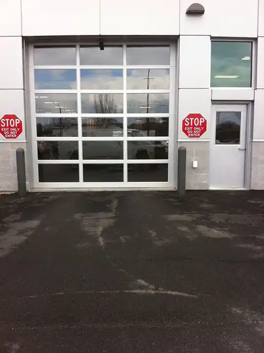 Full-view glass and aluminum commercial sectional door with a stop sign at left