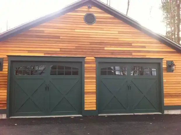 Two green X-brace doors with arched windows under natural cedar siding