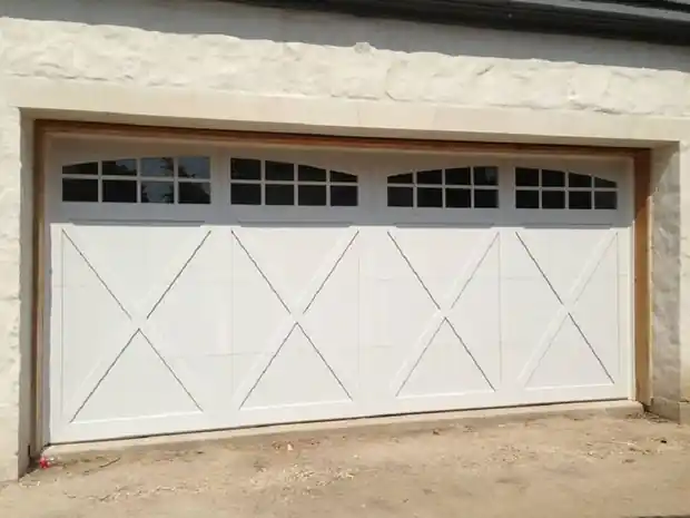 Wide white X-brace door with an arched window row under a stone lintel