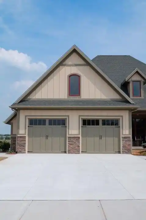 Two grey-green carriage doors on a new stone-and-shingle house