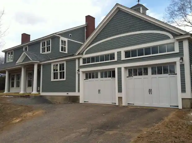 Two white carriage doors on a large grey-green house with a mud drive
